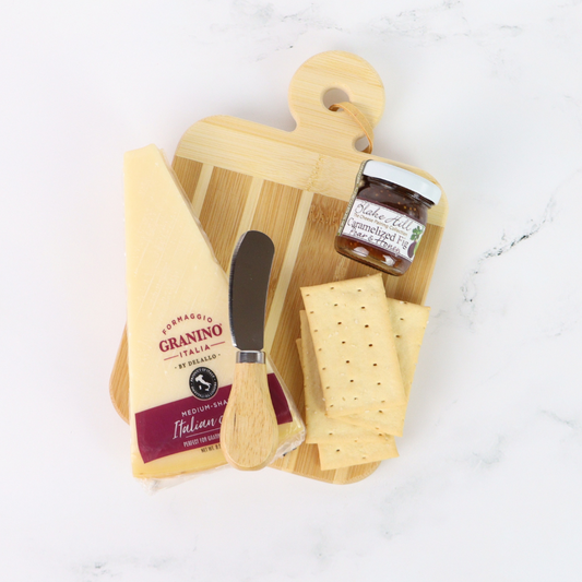 Wooden cutting board with cheese, a knife, and a jar of jam on a white surface