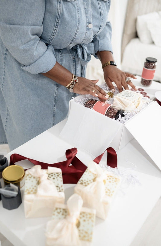 Sugarberry team member thoughtfully arranging a luxury custom gift box with artisan products and burgundy ribbon