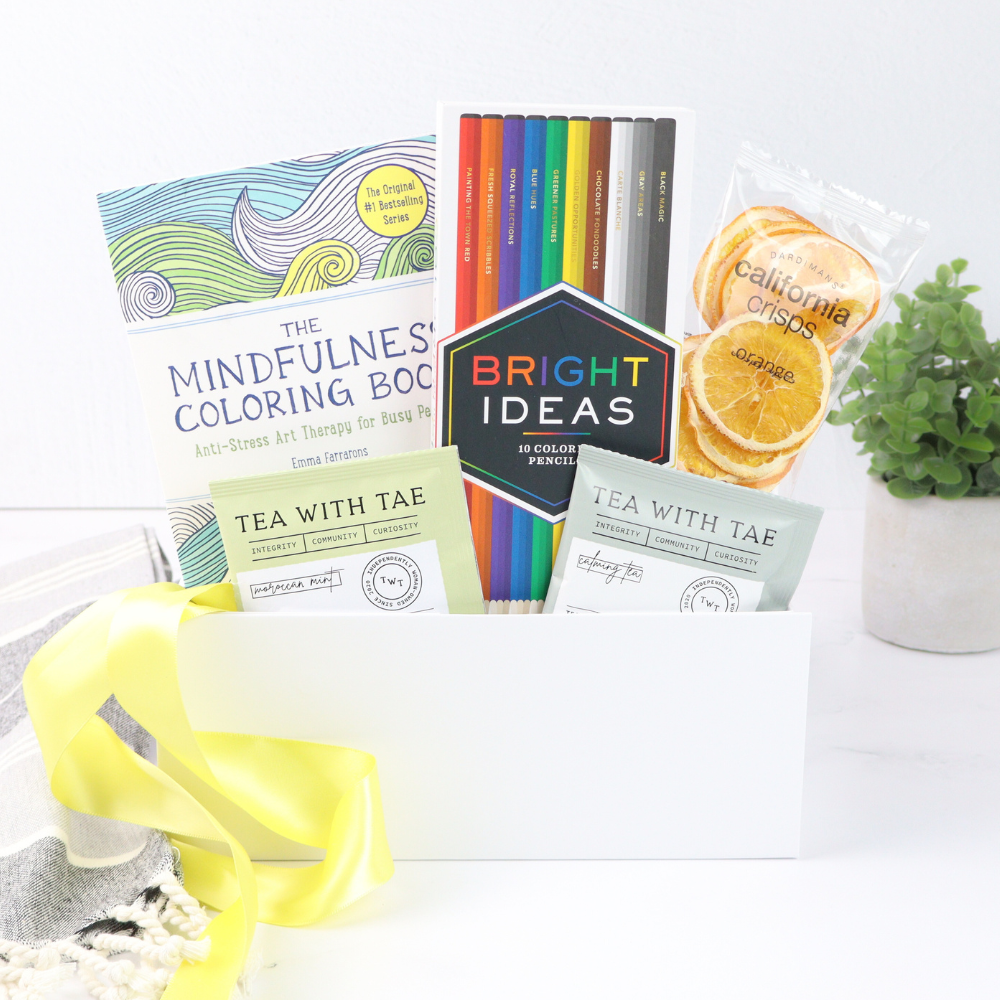 Colorful items including a mindfulness coloring book, tea packages, and a plant on a white surface.