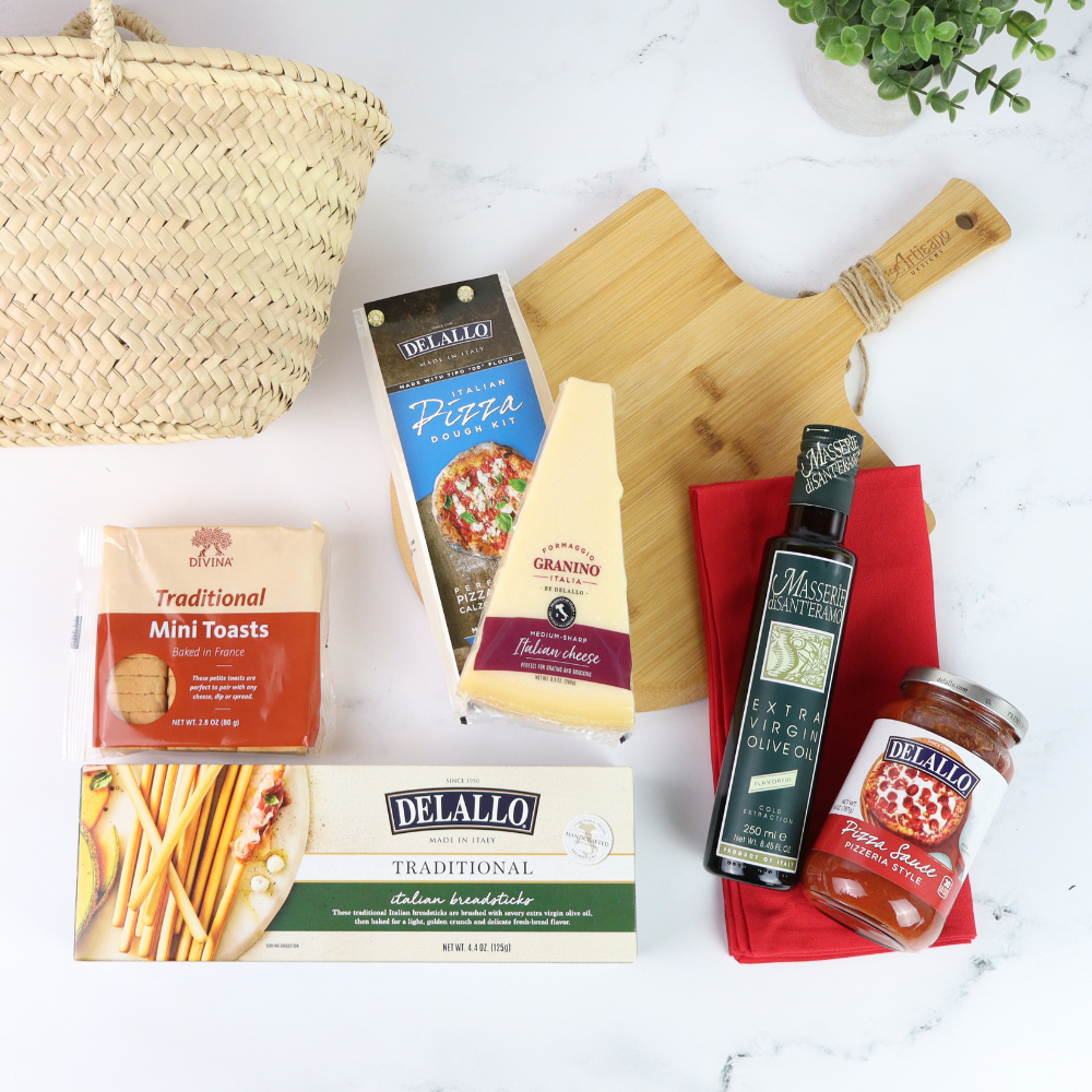 Assorted Delallo food products including pasta, cheese, and olive oil on a white surface with a basket and cutting board.