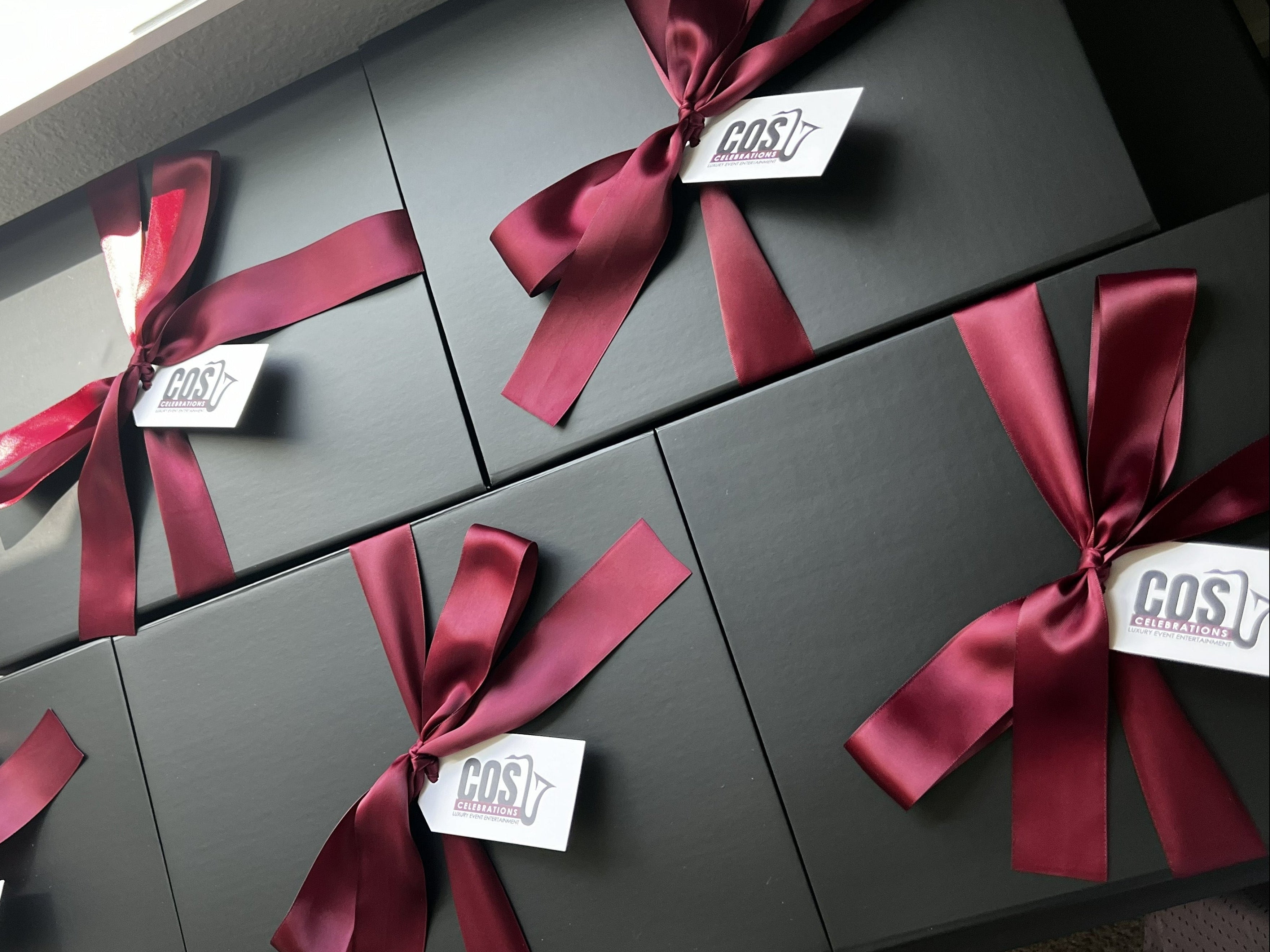 Set of black gift boxes with red ribbons and 'COS' tags on a neutral background