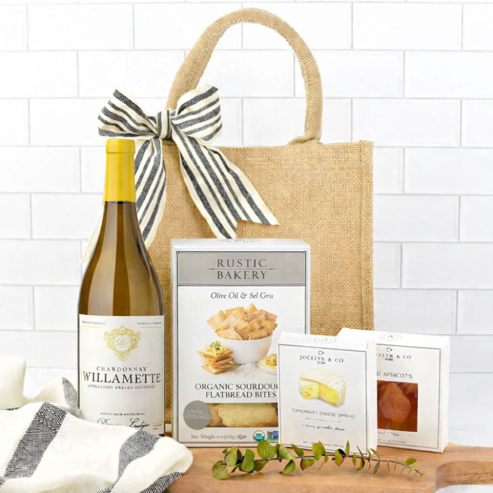 Gift basket with Willamette Chardonnay, Rustic Bakery items, and a decorative bow on a white tiled background.