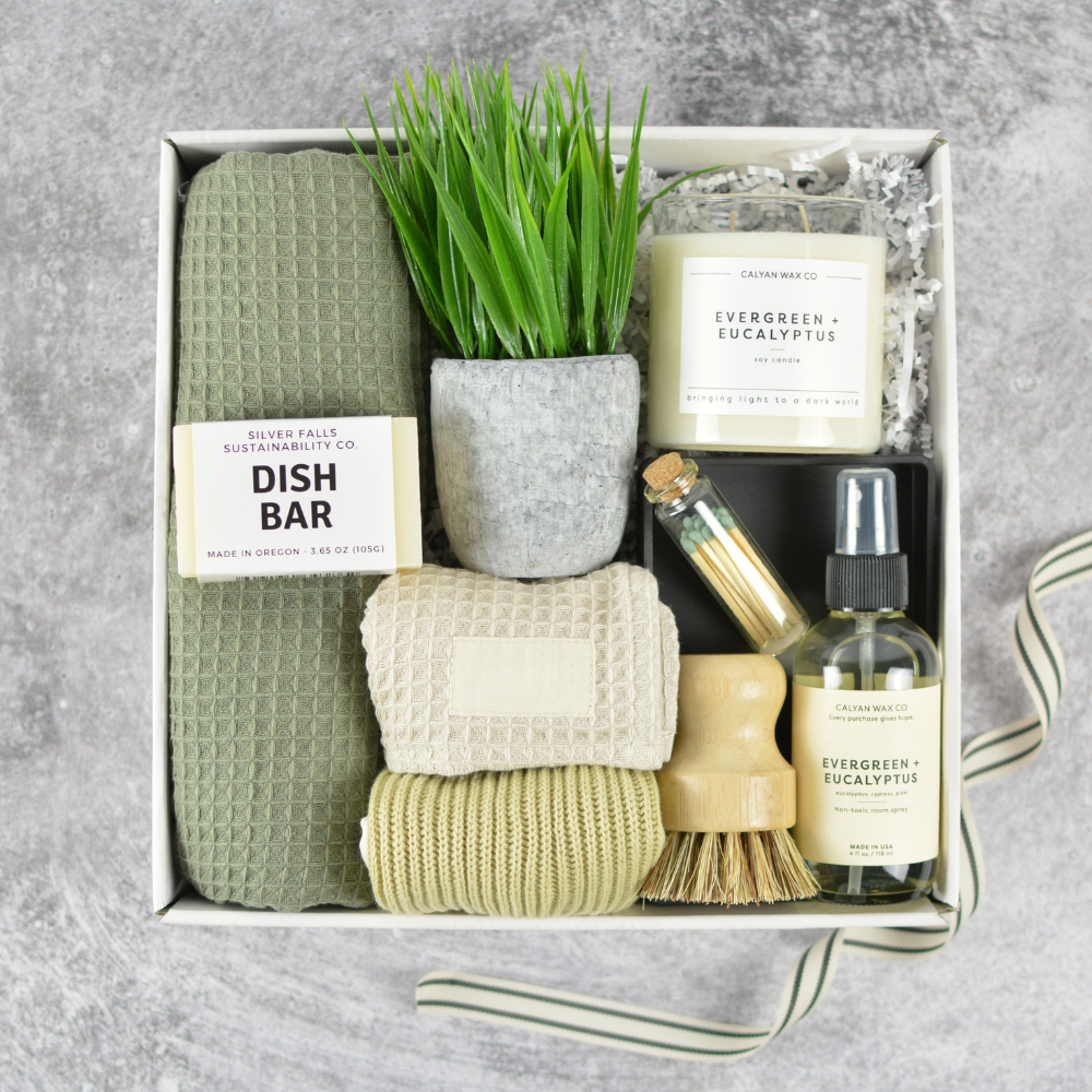 kitchen themed gift box for housewarming including a dish bar, plant, kitchen towels, candle and room spray in a box on a gray background