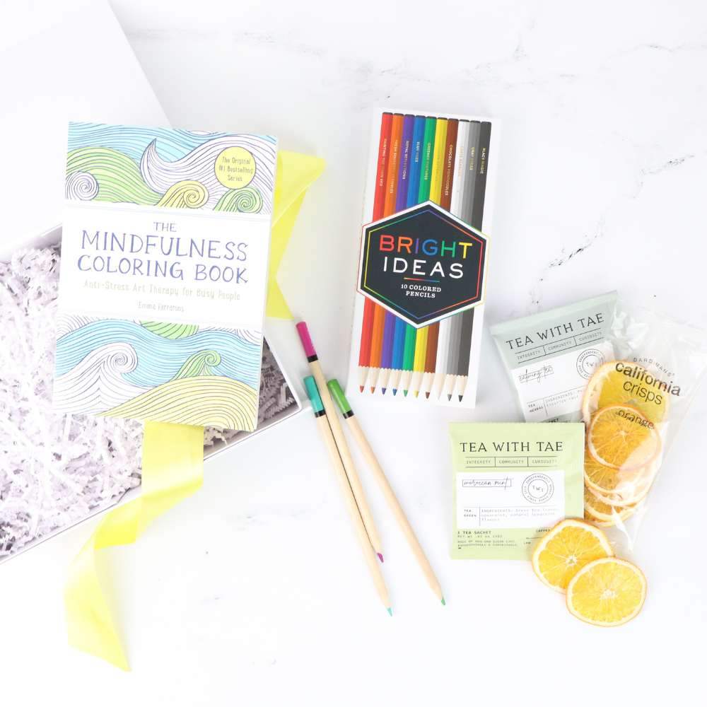 Coloring book, colored pencils, tea packages, and lemon slices on a white surface